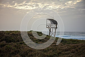 Lifeguard tower in a field surrounded by the sea under a cloudy sky in the evening