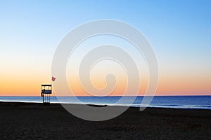 Lifeguard tower with red flag on beach in early morning