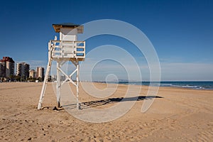 Lifeguard watch tower on empty beach with Gandia in background