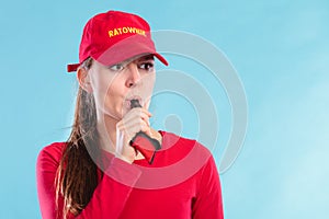 Lifeguard woman in cap on duty blowing whistle.