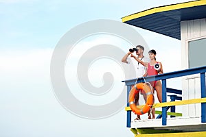 Lifeguards with megaphone and binocular on watch tower against blue sky