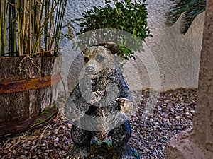 Lifelike damaged bear statue in a dynamic pose beside bamboo and shrubs in well-maintained garden