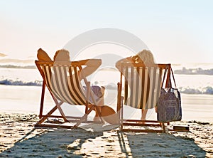 Lifes a beach. a couple admiring the sunset while seated on beach loungers.