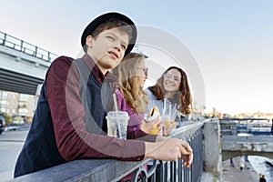 Lifestyle of adolescents, boy and two teen girls are walking in the city. Laughing, talking children eating street food, having photo