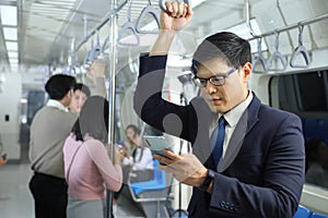 A lifestyle of Asian man wearing formal using cellphone while taking the subway train to work at the rush hour morning
