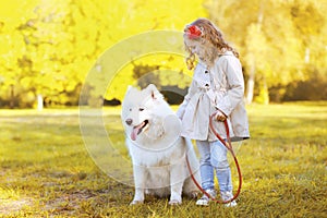 Lifestyle autumn photo, little girl and Samoyed dog walking in t