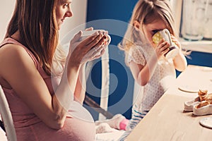 Lifestyle capture of pregnant mother and baby girl having breakfast and drinking tea at home photo