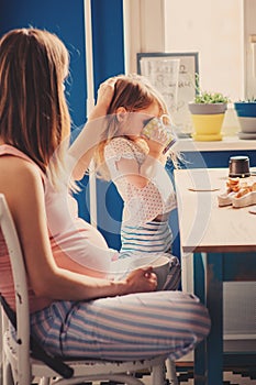 Lifestyle capture of pregnant mother and baby girl having breakfast at home