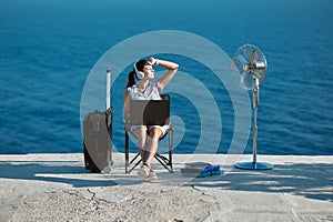 Lifestyle change idea. Business travelling concept. Happy woman in headset working on laptop, seascape on background.