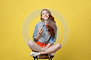 Lifestyle Concept: Pretty girl with long curly red hair enjoy listening to music on her phone and sitting on wooden