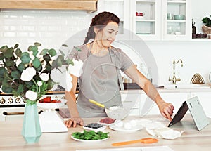 Lifestyle, cooking and freelance concept: Young woman looking at a recipe on her tablet and getting ready to make a cake