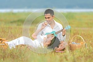 Lifestyle couple picnic sunny time. Asian young couple having fun and relax playing guitar on picnic in the meadow and field in ho