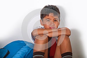 Young sad scared latin kid 8 years old in school uniform and backpack sitting alone crying depressed and frightened suffering abus