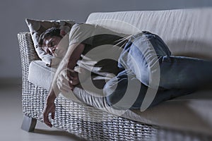 Lifestyle dramatic light portrait of young sad and depressed man lying at shady home couch in pain and depression feeling lost loo