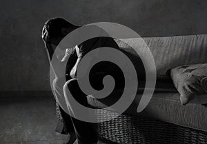 Lifestyle dramatic light portrait of young sad and depressed man sitting at shady home couch in pain and depression feeling stress