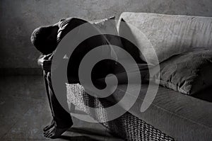 Lifestyle dramatic light portrait of young sad and depressed man sitting at shady home couch in pain and depression feeling stress