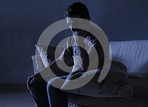 Lifestyle dramatic light portrait of young sad and depressed man sitting at shady home couch in pain and depression feeling lost l