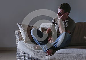 Lifestyle dramatic light portrait of young sad and depressed man sitting at shady home couch in pain and depression feeling lost l