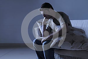 Lifestyle dramatic light portrait of young sad and depressed man sitting at shady home couch in pain and depression feeling lost l