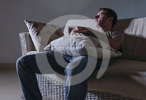 Lifestyle dramatic light portrait of young sad and depressed man sitting at shady home couch in pain and depression feeling lost l