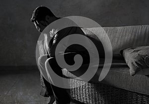 Lifestyle dramatic light portrait of young sad and depressed man sitting at shady home couch in pain and depression feeling stress