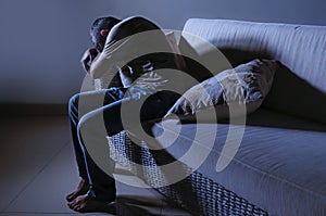 Lifestyle dramatic light portrait of young sad and depressed man sitting at shady home couch in pain and depression feeling stress