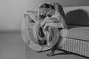 Lifestyle dramatic light portrait of young sad and depressed man sitting at shady home couch in pain and depression feeling stress