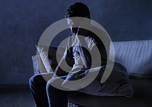 Lifestyle dramatic light portrait of young sad and depressed man sitting at shady home couch in pain and depression feeling stress