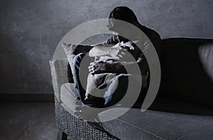 Lifestyle dramatic light portrait of young sad and depressed man sitting at shady home couch in pain and depression feeling stress