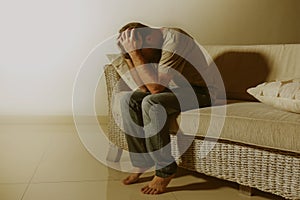 Lifestyle dramatic light portrait of young sad and depressed man sitting at shady home couch in pain and depression feeling stress