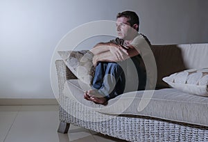 Lifestyle dramatic light portrait of young sad and depressed man sitting at shady home couch in pain and depression feeling stress