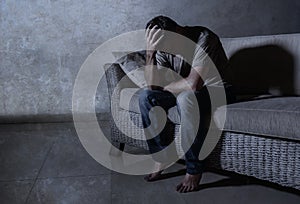 Lifestyle dramatic light portrait of young sad and depressed man sitting at shady home couch in pain and depression feeling stress