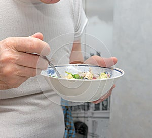 Lifestyle elderly man dine at home picking fresh salad with a fork. The man eats at the table. Lunch