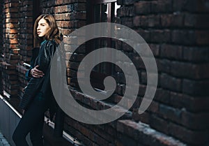 Lifestyle fashion portrait of brunette girl in rock black style, standing outdoors in the city street