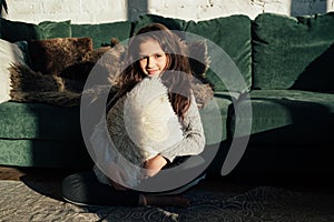 Lifestyle fashion portrait of young stylish hipster child girl sitting near sofa, wearing cute trendy outfit, smiling enjoy weeken