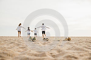 lifestyle father, mother and kids take off shoes running on sand
