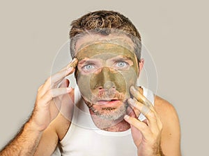 Attractive and surprised funny man horrified looking himself on bathroom mirror ugly and weird applying green cream on his face i