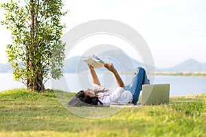 Lifestyle Girl enjoy listening music and reading a book and play laptop on the grass field of the nature park in the morning gree