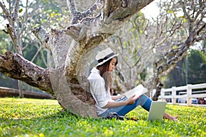 Lifestyle Girl enjoy listening music and reading a book and play laptop on the grass field of the nature park in the morning gree