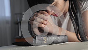 Lifestyle girl praying indoors at bedtime on bible. Religion concept evening prayer woman brunette hands on bible