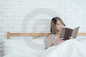 Lifestyle happy young Asian woman enjoying lying on the bed reading book pleasure in casual clothing at home.