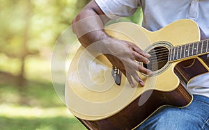 Lifestyle hobbies concept. Hands of guy playing acoustic guitar while sitting on nature background. Handsome man practicing