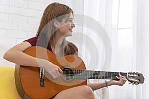 Lifestyle hobby leisure entertainment concept. Casual young woman playing acoustic guitar while sitting on white sofa in living