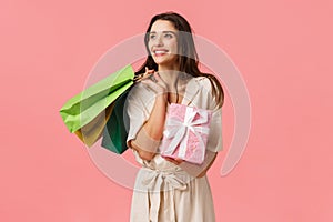 Lifestyle, holidays and emotions concept. Cheerful carefree young feminine woman holding shopping bags and wrapped cute