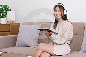 Lifestyle at home concept, Young Asian woman is listening music and surfing social media on tablet
