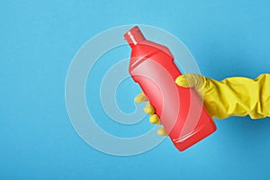 Lifestyle home keeping concept. hand in rubber glove holds red bottle with washing gel. Detergent bottle without label