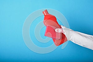 Lifestyle home keeping concept. hand in rubber glove holds red bottle with washing gel. Detergent bottle without label