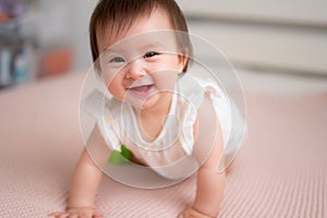 lifestyle home portrait of 9 months old mixed ethnicity Asian Caucasian baby girl playing happy and carefree on bed crawling and