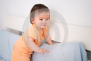 lifestyle home portrait of adorable and beautiful 9 months old baby girl learning to stand up by holding bed frame smiling