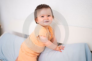 lifestyle home portrait of adorable and beautiful 9 months old baby girl learning to stand up by holding bed frame smiling